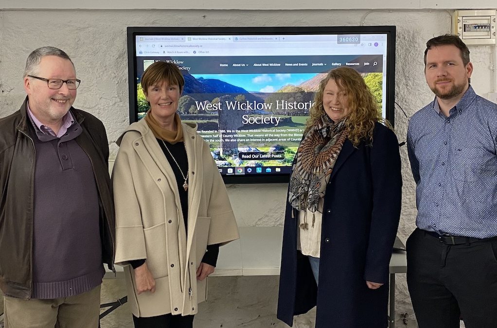 At the West Wicklow Historical Society Launch 3 of the 4 website sub committee members, Paul Gorry, Cora Crampton and Declan Keenan, with Rachel Kane stand in front of the website on the big screen behind them showing the website at the launch